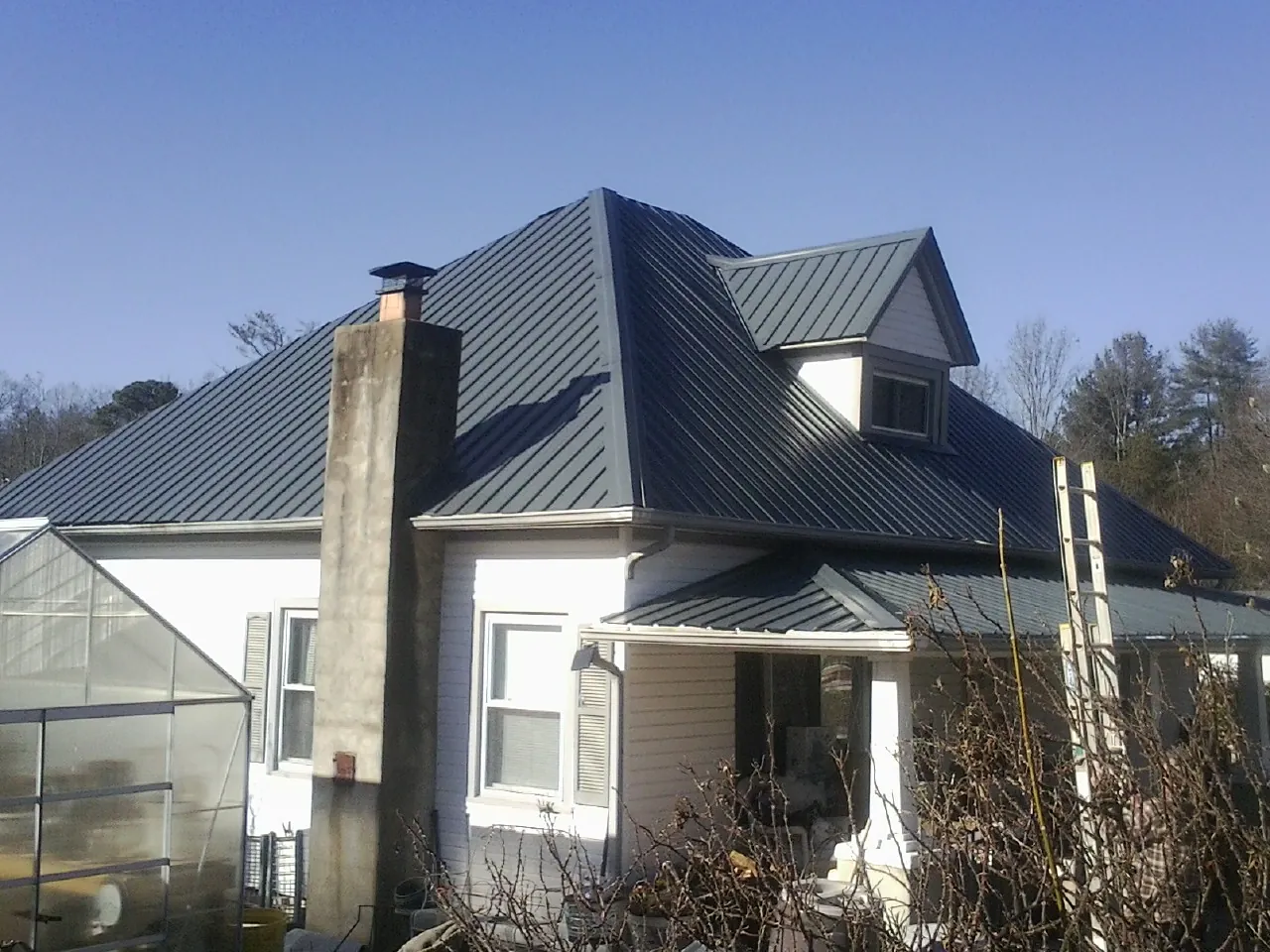 Dark blue standing seam metal roof on a white farmhouse with dormer — Slate & Tile Roof Repair by Roofing Brothers in Howells