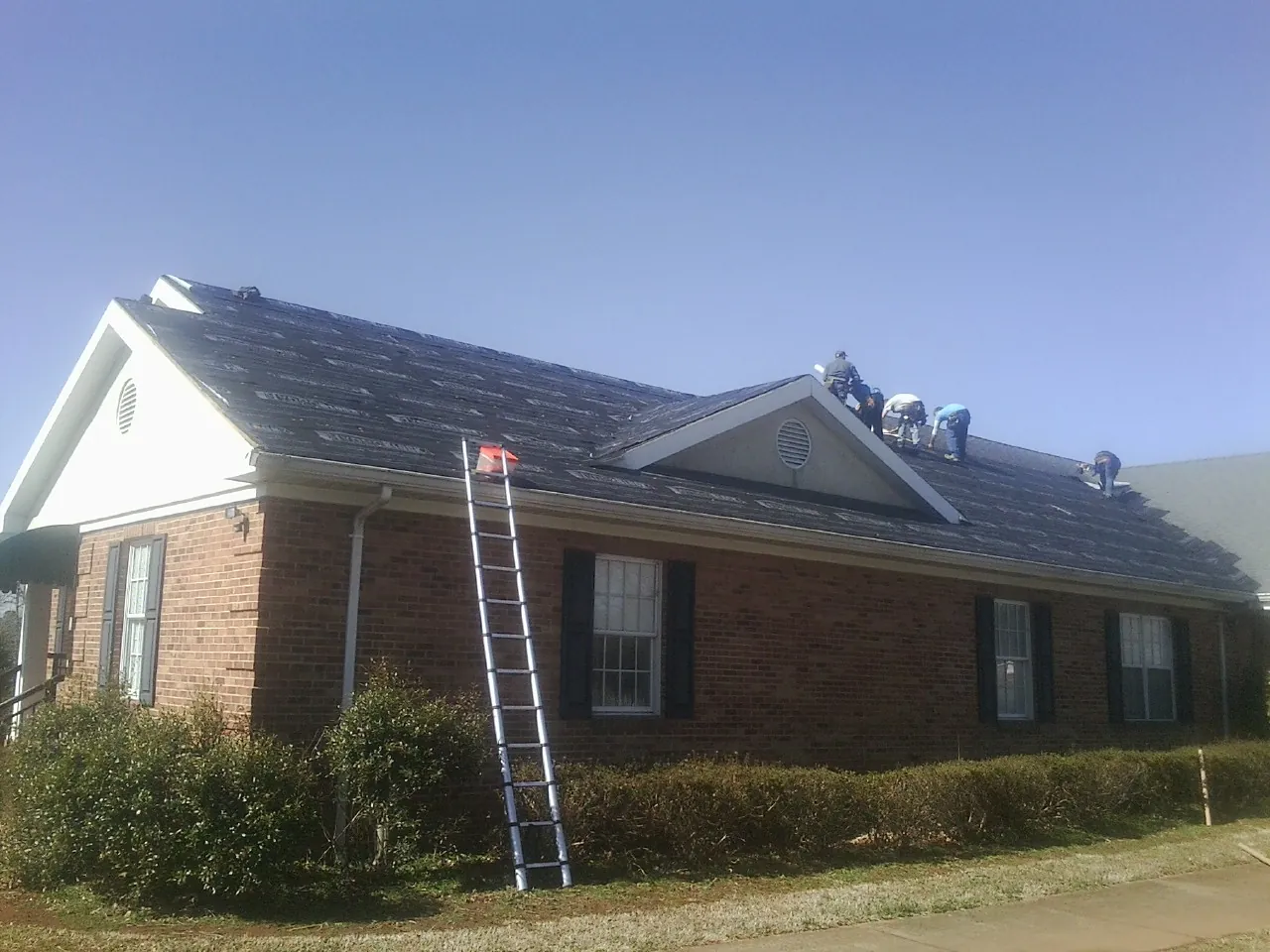 Crew tearing shingles off a brick ranch roof with a ladder set — Emergency Roof Repair work by our crew in Howells