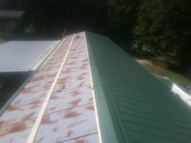 Old rusted panels beside newly installed green metal roofing — Wind Damage Roof Repair by Roofing Brothers in Howells