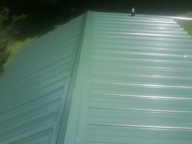 New green metal panels meeting at the ridge of a roof — Flat Roof Repair work by our crew in Howells
