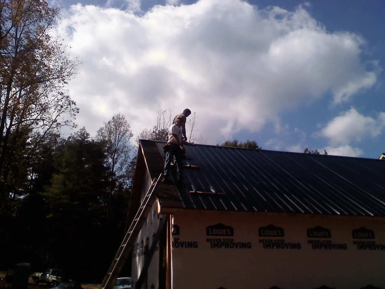 Roofer fastening dark metal panels high against a cloudy sky, from a Roof Inspection job in Howells