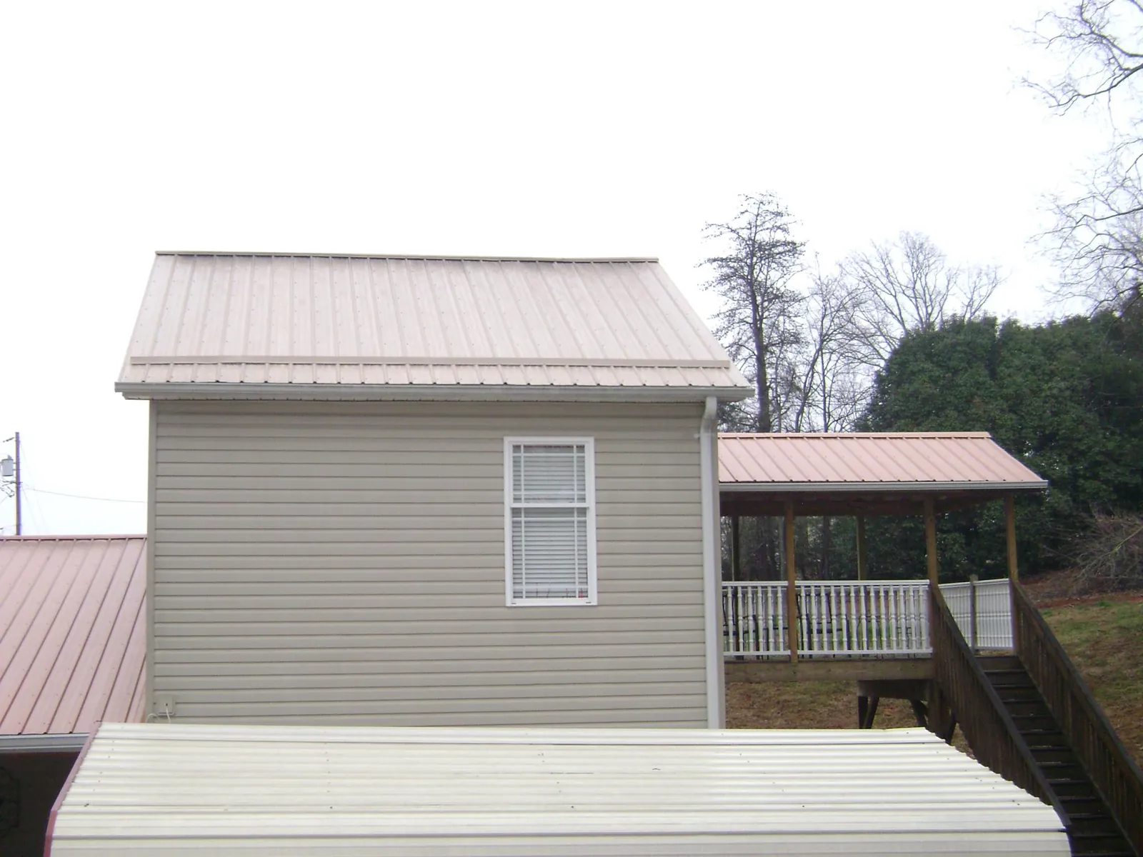 Tan metal roofs on a two story addition and attached porch, from a Roof Replacement job in Howells